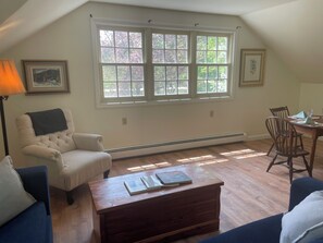 A living room with a large window, a chair, a coffee table, and a dining table with chairs. - Charming studio with WiFi and AC in gorgeous St. Albans (St.Albans)