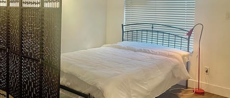 A bedroom with a bed, a window with blinds, a ceiling fan, and a floor lamp.