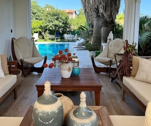 Une pièce lumineuse donnant sur la piscine, avec deux canapés beige, une table basse en bois et des vases décoratifs.
