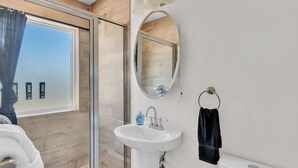 Een badkamer met een douchecabine van glas, een wit wastafelmeubel, een spiegel en een handdoekhouder.