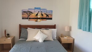 Een slaapkamer met een bed, nachtkastjes, een plafondventilator en een schilderij van giraffen aan de muur.