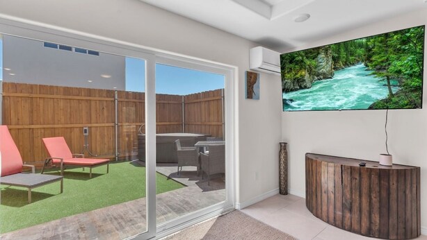 Een moderne woonkamer met een glazen deur naar een patio, een houten receptiebalie en een grote televisie aan de wand.