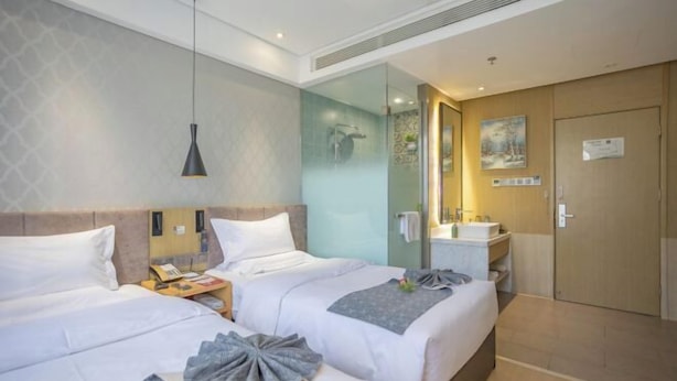 Ein Hotelzimmer mit zwei Betten, einem Nachttisch mit Lampe, einem Badezimmer mit Spiegel und einer Tür mit einem Schild.
