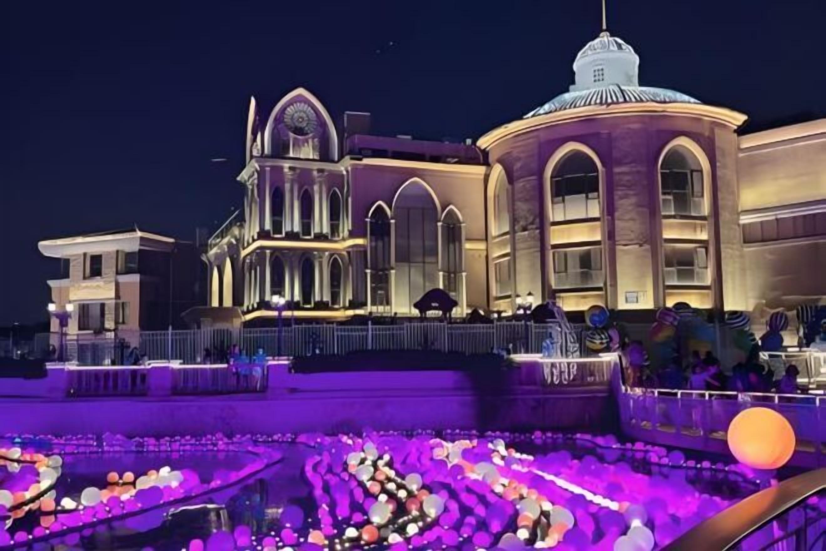 A building with arched windows and a dome, surrounded by a water feature with floating lights.