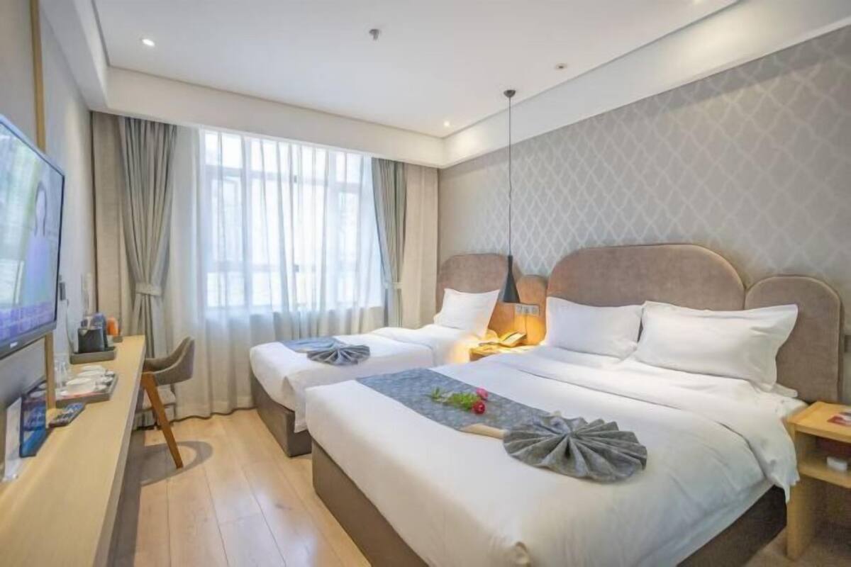 A hotel room with two beds, a TV, a desk, and a window with curtains.