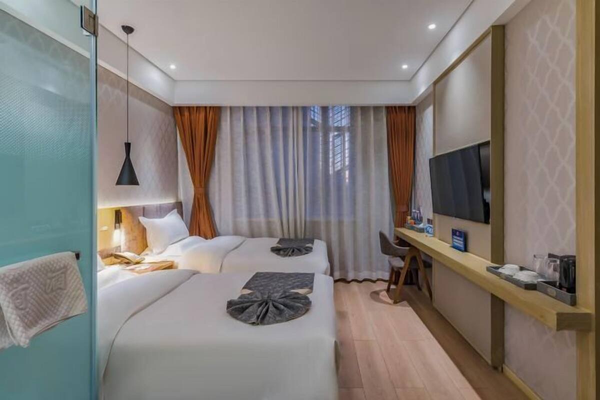 A hotel room with two beds, a desk, a TV, and a window with curtains.