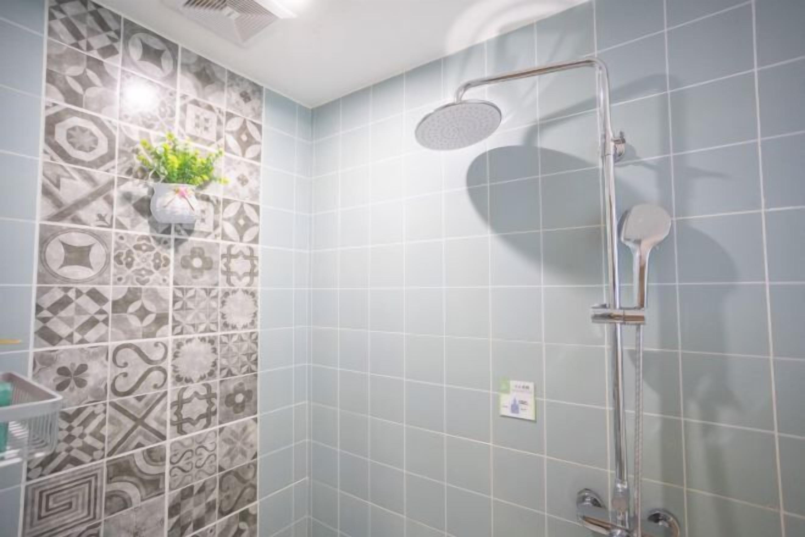 Een badkamer met betegelde muren, een douche met handdouche en een kleine plant in een pot op de muur.
