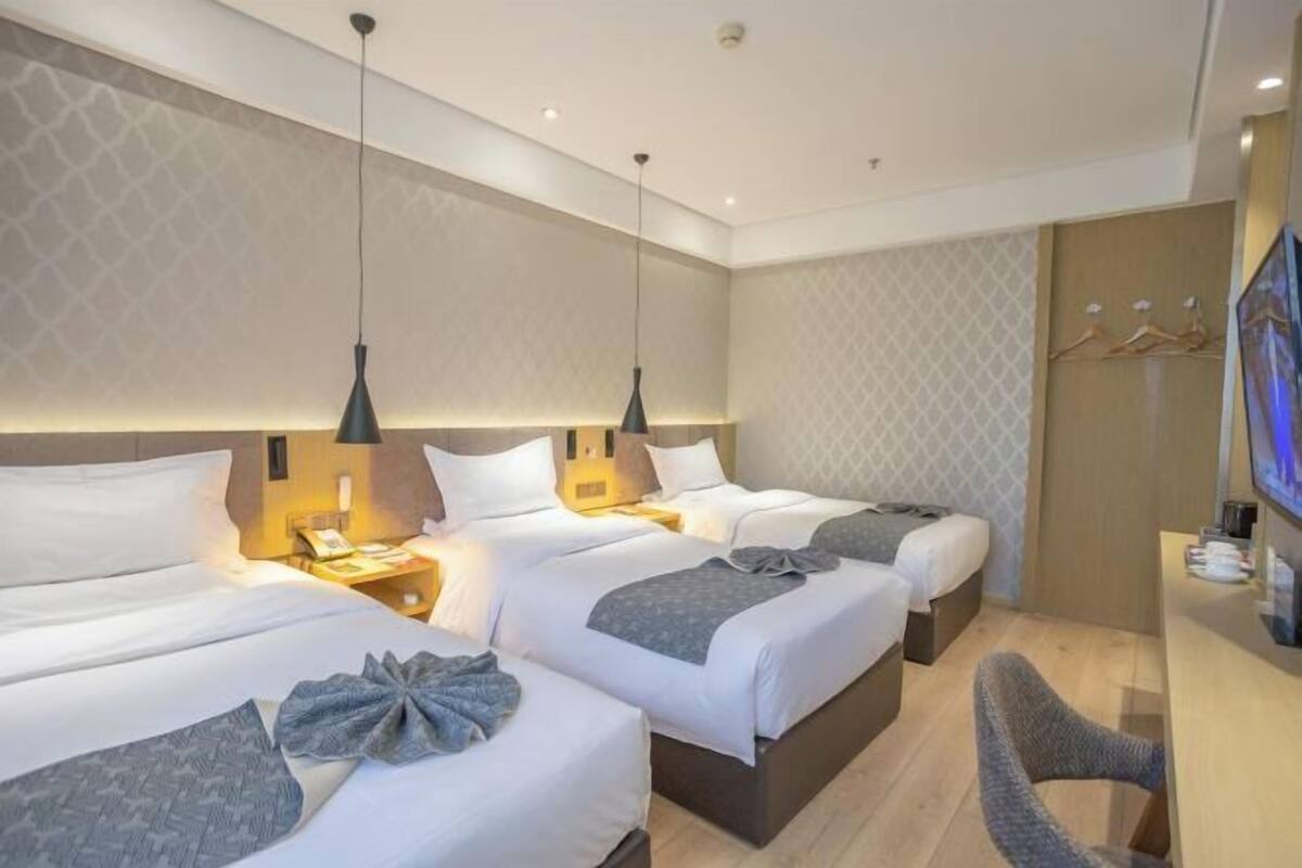 A hotel room with two beds, a desk, a chair, and a TV.