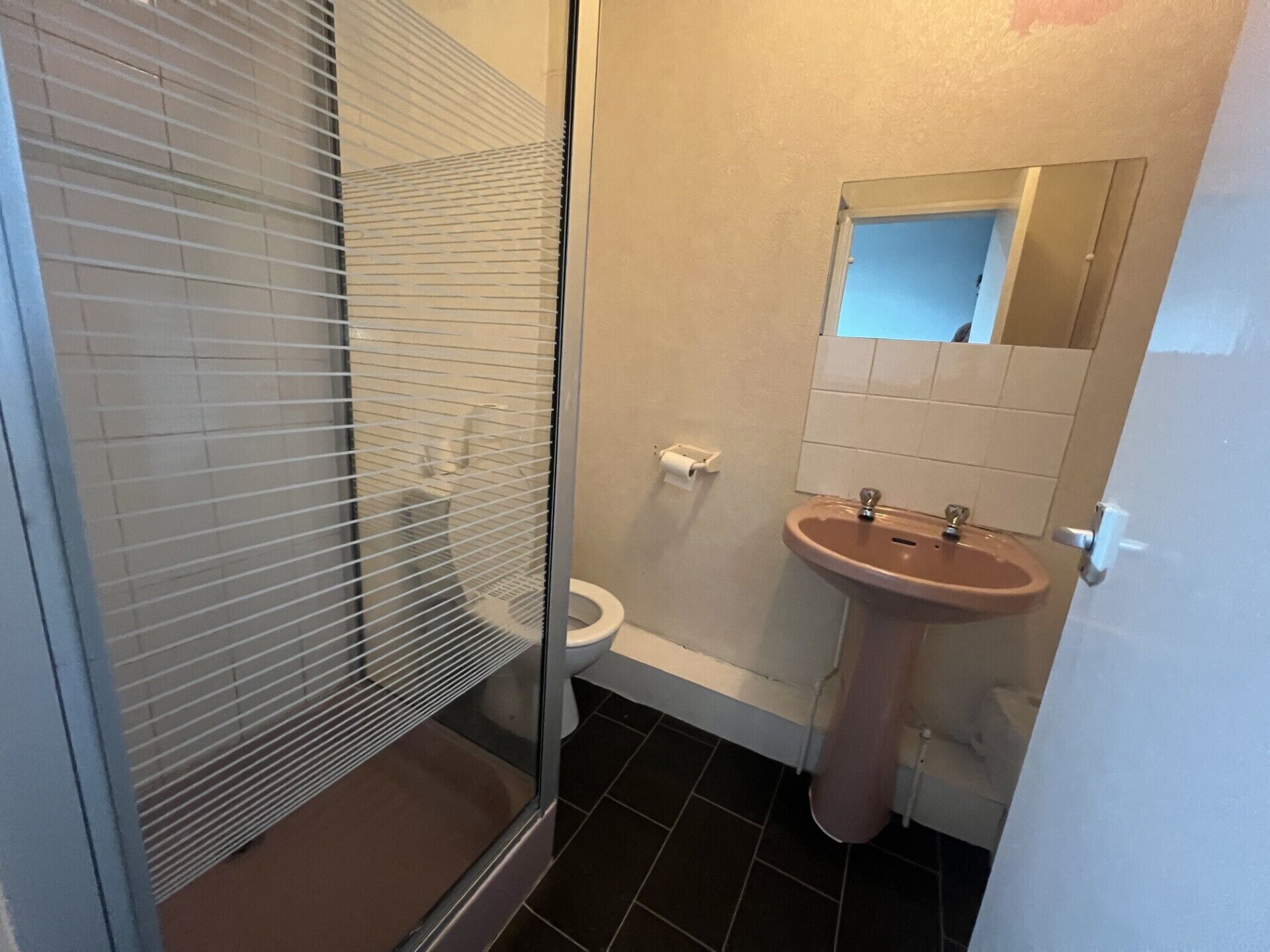 Et badeværelse med toilet, håndvask og bruseområde med glasdør.