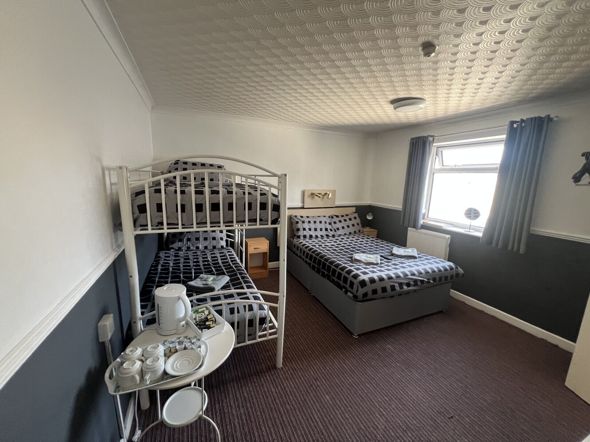 A room with bunk beds, a small table with a kettle, and a window with curtains.