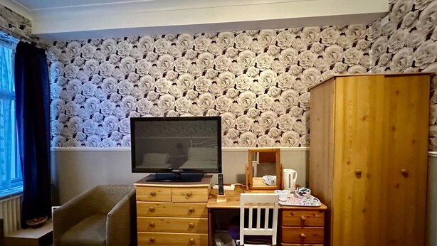 A hotel room with a television, wooden furniture, a desk, and a wardrobe. - The AVON Hotel (Blackpool)