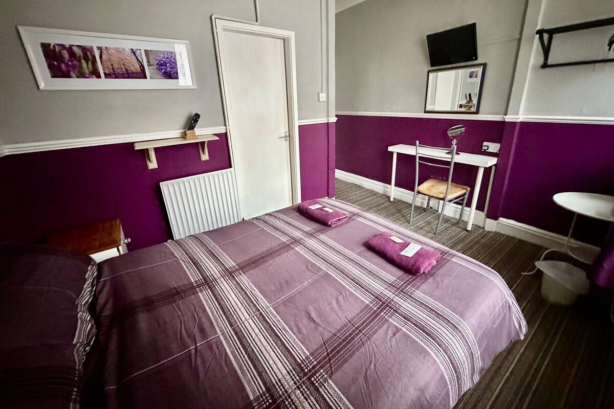 A bedroom with a bed, a desk, a chair, and a television on the wall.