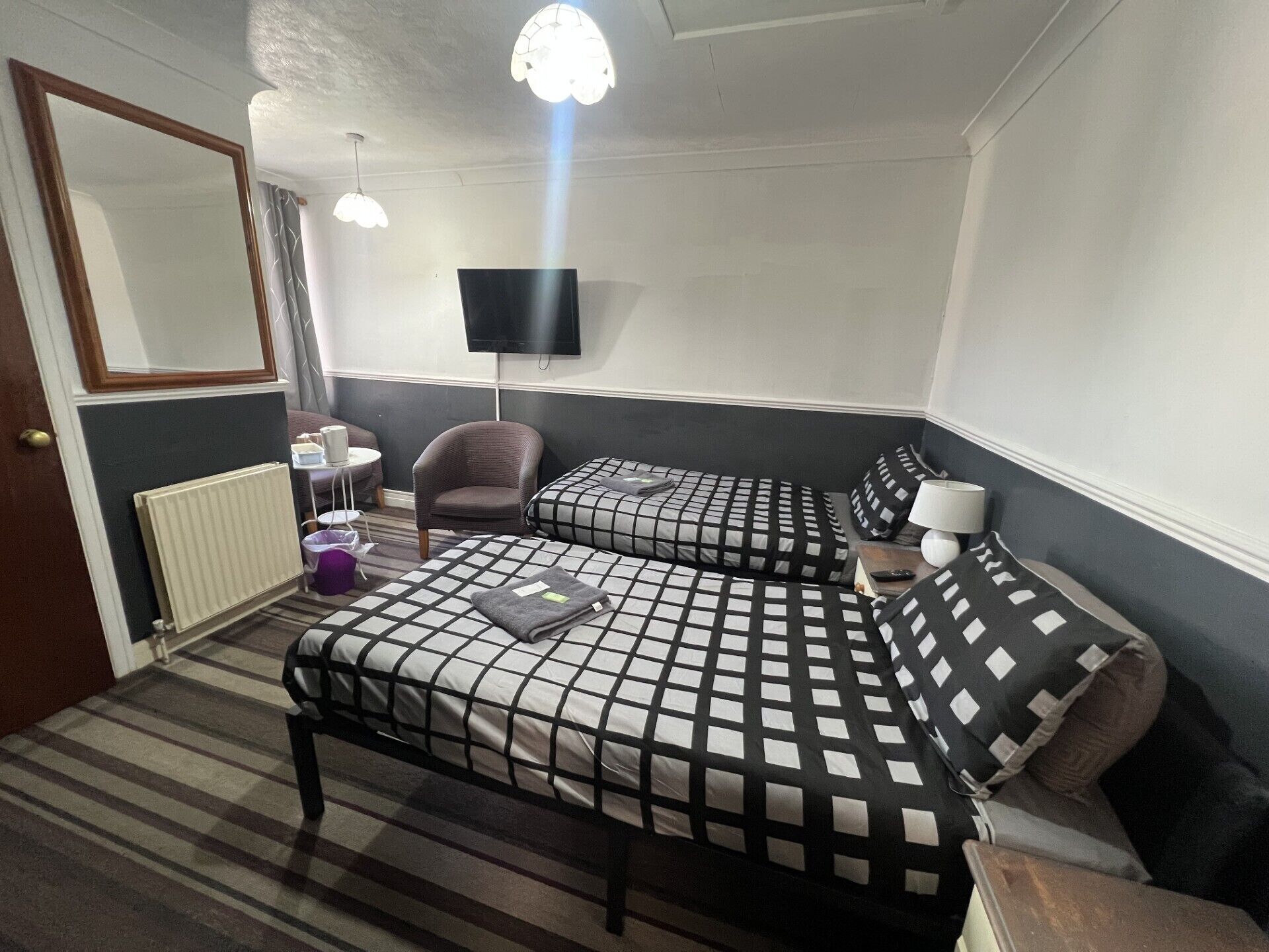 Une chambre d’hôtel avec deux lits, une chaise, une petite table, un téléviseur et un radiateur.