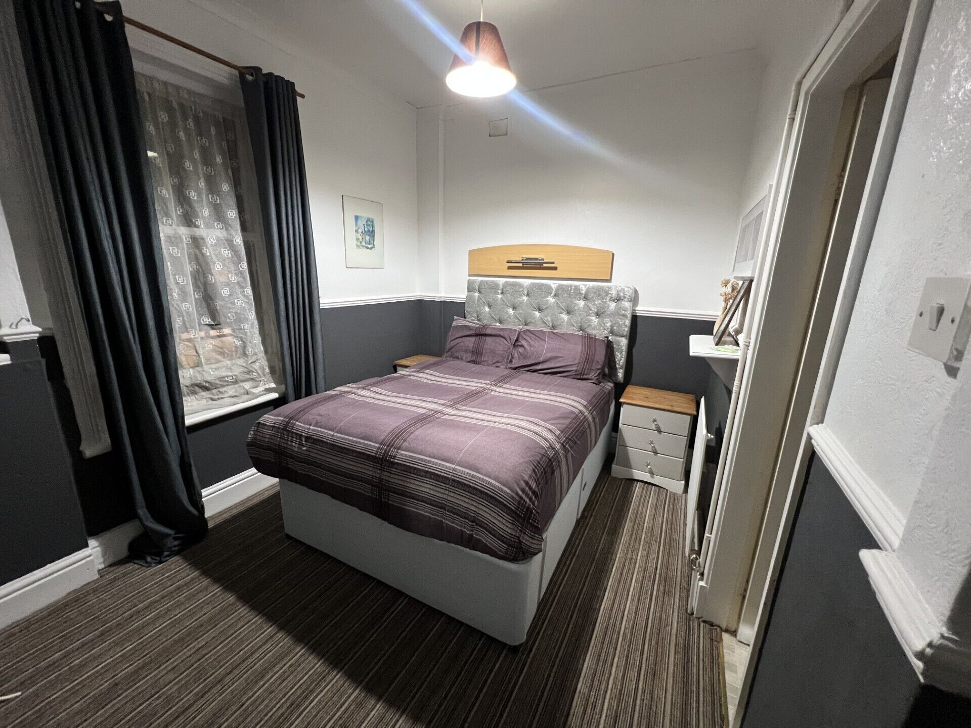A bedroom with a bed, a nightstand, a window with curtains, and a hanging light fixture.