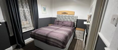 A bedroom with a bed, a nightstand, a window with curtains, and a hanging light fixture.