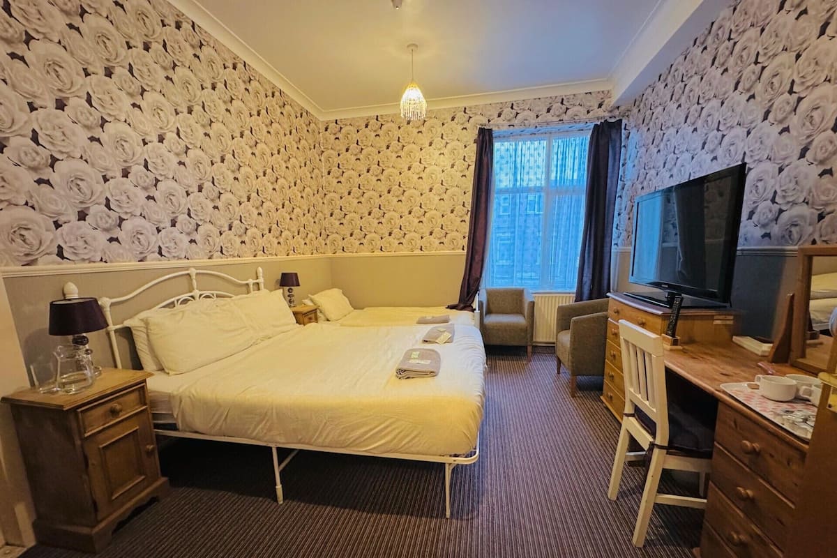 A hotel room with two beds, a television, a desk with a chair, and a window with curtains.