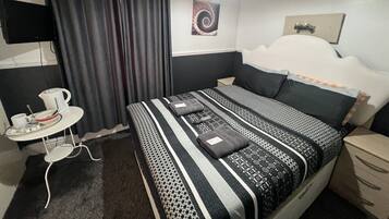 Habitación de hotel ordenada con una cama, una mesita con un hervidor y un televisor montado en la pared.