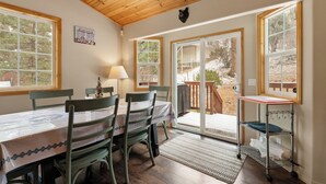 Un comedor con una mesa dispuesta para cuatro, sillas de madera, una lámpara y vistas al exterior a través de amplios ventanales.