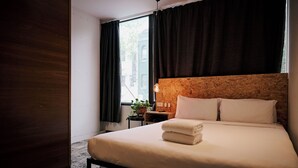 A hotel room with a bed, a bedside table, a potted plant, and a window with curtains.