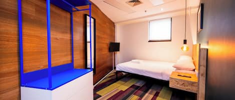A modern hotel room with a bed, a small desk, a chair, and a window.