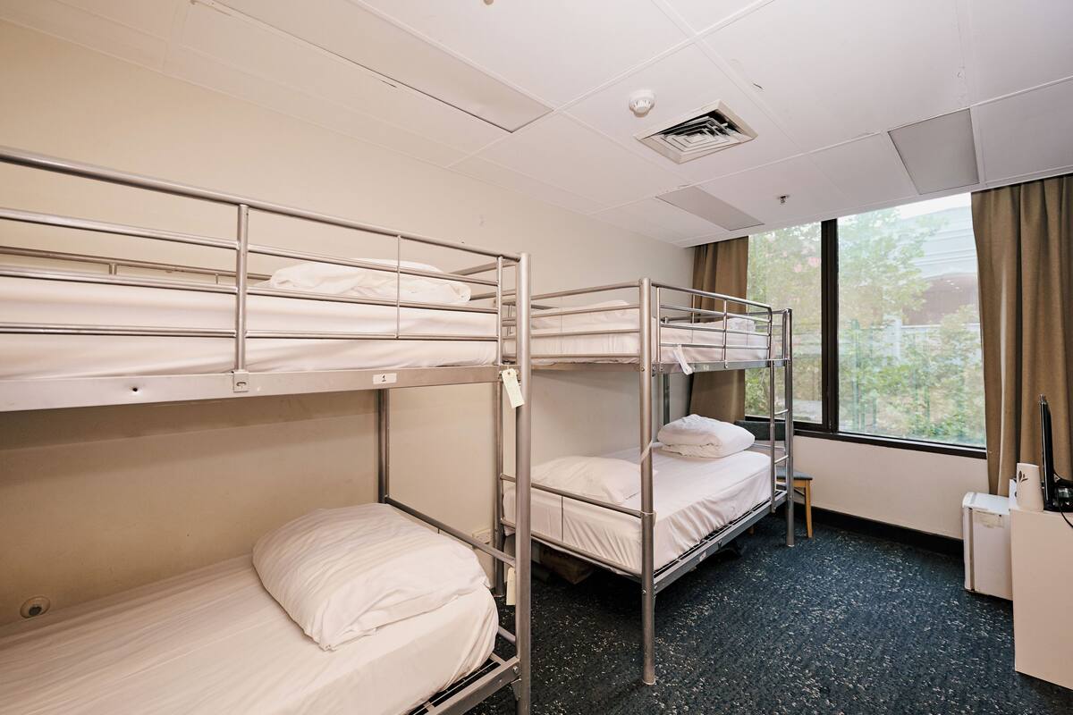 Habitación de hotel con literas, un escritorio, una silla y una ventana con cortinas.