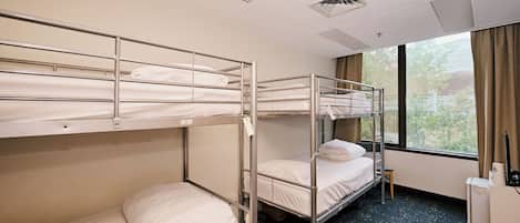 A hotel room with bunk beds, a desk, a chair, and a window with curtains.
