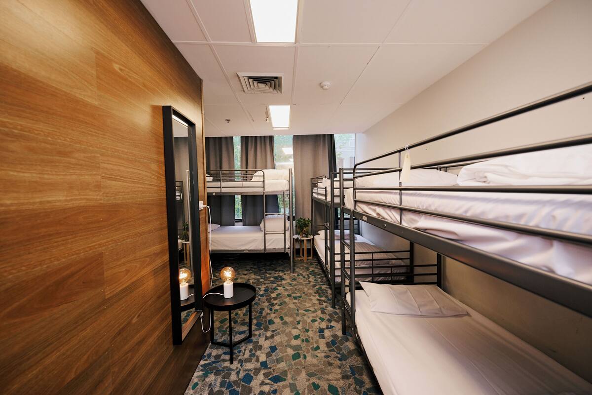 Habitación de hotel con literas, una pequeña mesa redonda con lámpara, un espejo y vistas al exterior.