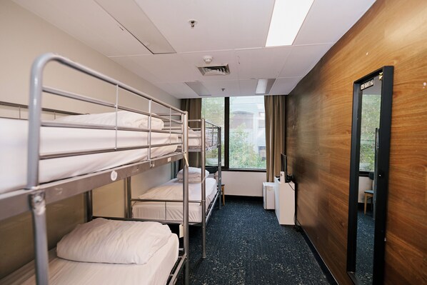 A bunk room with metal bunk beds, a small table, a chair, and a window with a view of greenery.