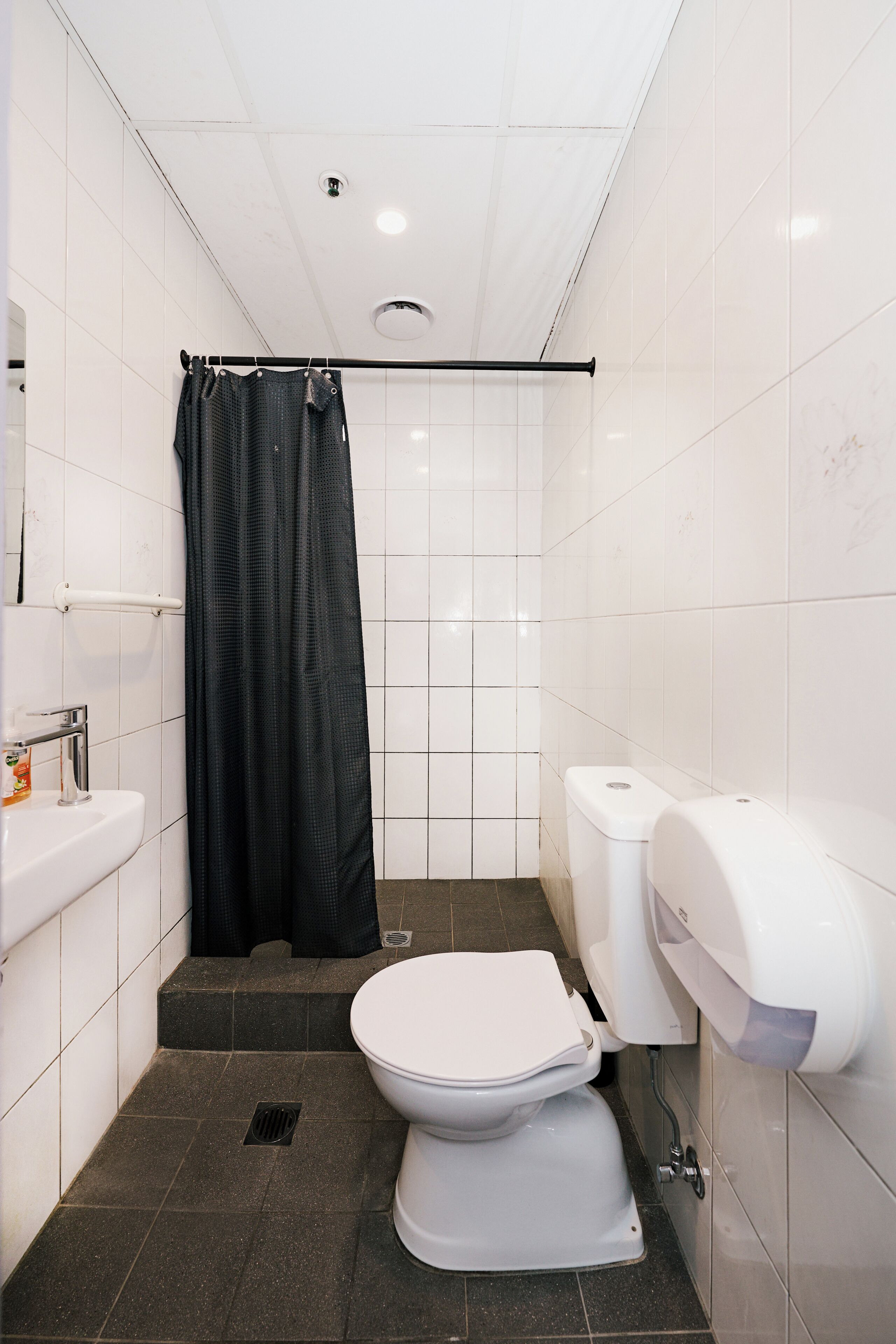 Un baño pequeño con inodoro blanco, cortina de ducha negra, lavabo blanco y dispensador de toallas de papel.
