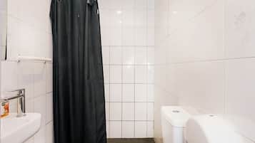 A compact bathroom with a white toilet, a black shower curtain, a white sink, and a paper towel dispenser.