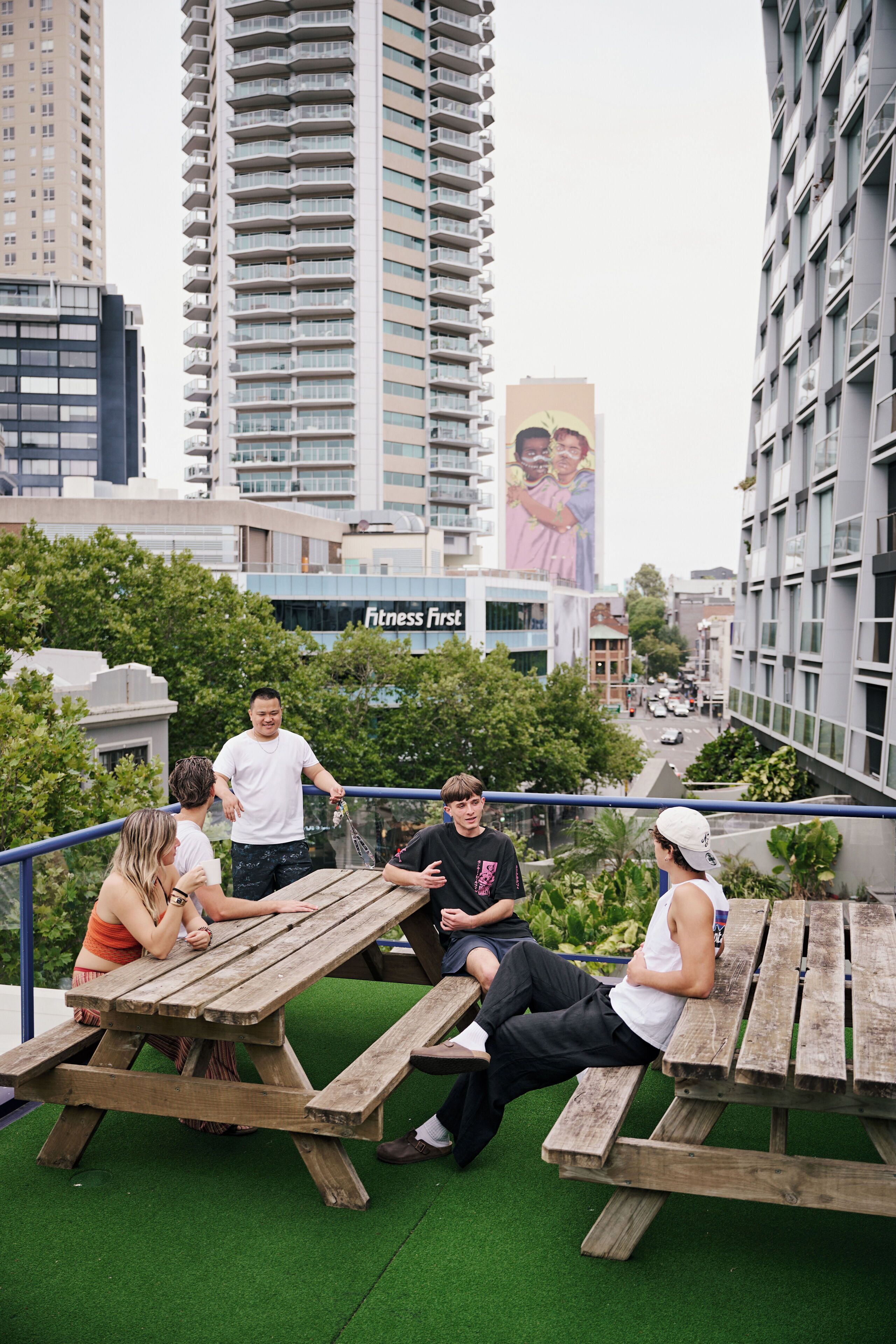 A group of people sitting at a wooden picnic table on a rooftop with a cityscape view.