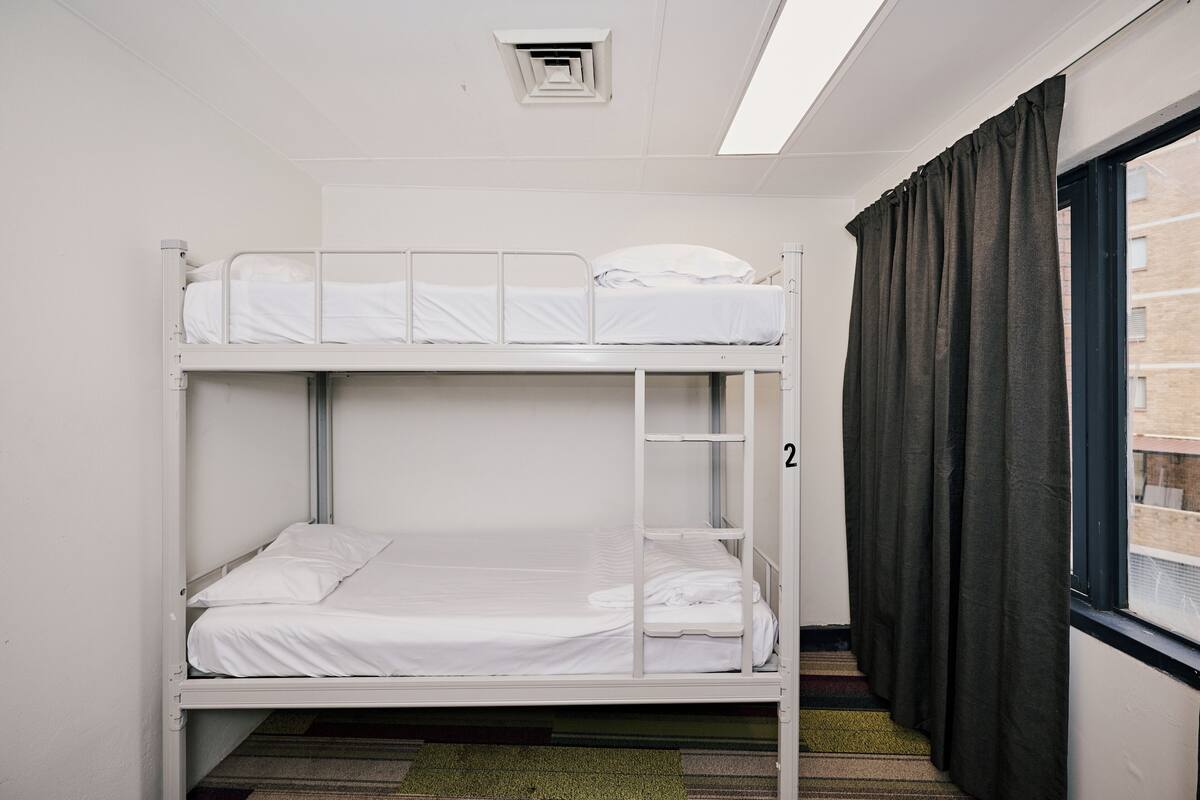 Dormitorio con literas, ventana, cortinas y piso alfombrado.