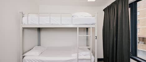 A bunk bed room with a window, curtains, and a carpeted floor.