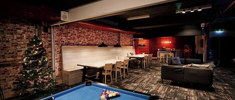 A pool table with balls, a Christmas tree, and a bar area with stools and a counter.