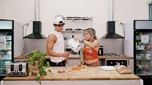 A kitchen with a wooden countertop, a toaster, a plant, and a person pouring a liquid.