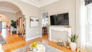 A spacious living room with a fireplace, a television mounted above it, and a dining area visible through an archway.