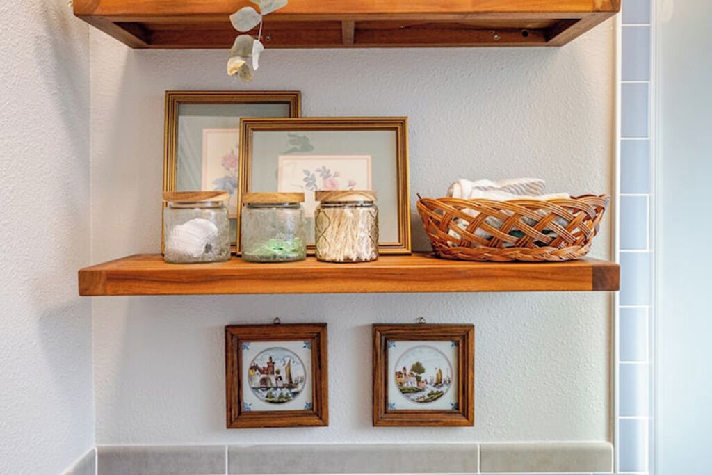 A wooden shelf with jars, framed pictures, and a woven basket.