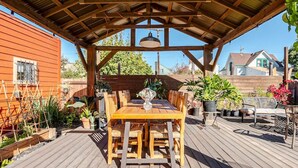 A wooden deck with a covered patio area, a wooden table with chairs, and potted plants.