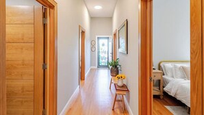 A hallway with wooden doors, a small table with a plant, and a bed in the background.