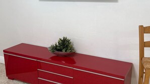 Et rødt underholdningscenter med et fladskærms-tv monteret på væggen, en lille plante ovenpå og en træstol til højre.