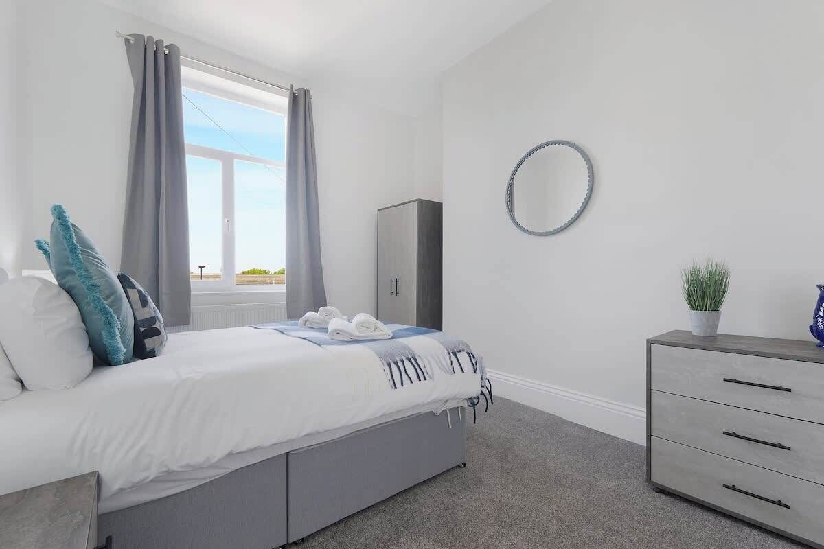A bedroom with a bed, a dresser, a mirror, and a window with curtains.
