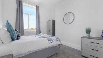 A bedroom with a bed, a dresser, a mirror, and a window with curtains.