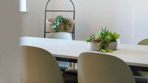 Una mesa de comedor con sillas, una planta en maceta y un estante de metal con una cesta.