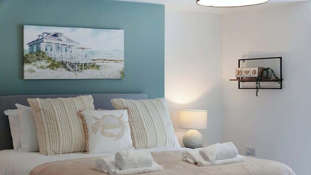 Un dormitorio con cama, almohadas, un cuadro, una mesita de noche y un estante en la pared.
