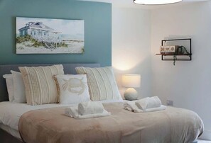 Une chambre à coucher avec un lit, des oreillers, un tableau, une table de chevet et une étagère fixée au mur.