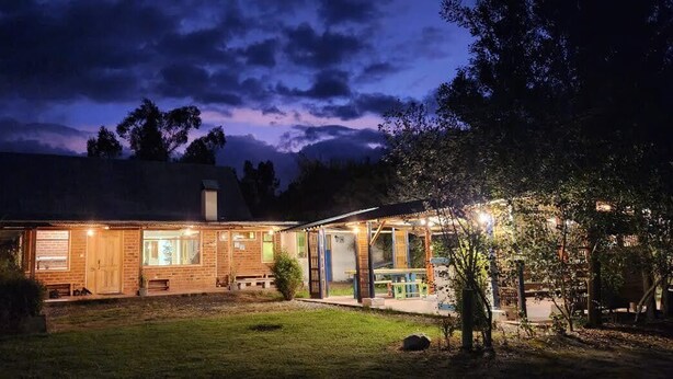 A two-story building with a brick facade, a covered porch, and a well-lit entrance. - Hosteria y Camping WiM (Machachi)