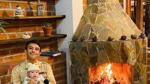 A man sitting in a living room with a stone fireplace, holding a child. - Hosteria y Camping WiM (Machachi)