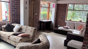 A spacious living area with two sofas, a small table, and a window with a view of greenery. - Hosteria y Camping WiM (Machachi)