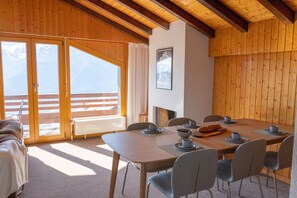 Ein Essbereich mit einem Holztisch, gedeckt für vier Personen, Stühlen, einem Buffet mit Brot und Blick auf Berge durch große Glastüren.