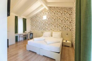 Un dormitorio con una cama, mesitas de noche, un escritorio y un papel tapiz estampado.